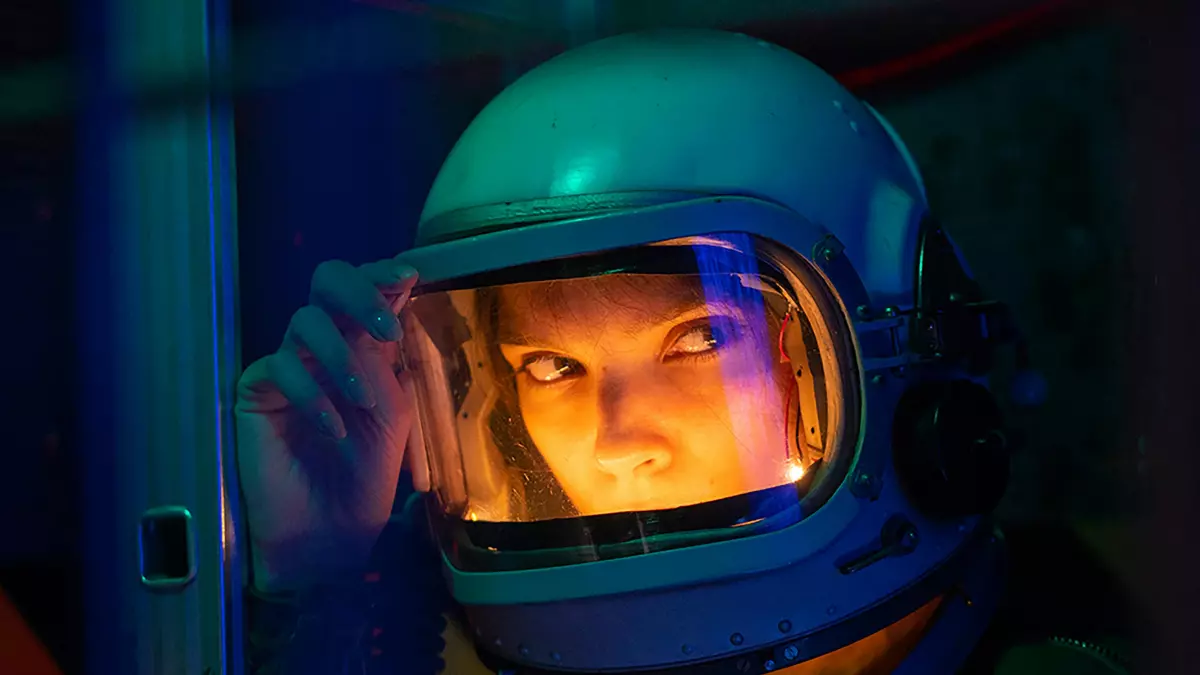 Close-up of a person wearing a futuristic astronaut helmet, illuminated with vibrant teal and orange light.