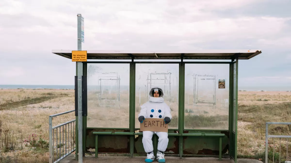 An astronaut in a white spacesuit stands on a barren, rocky landscape and holds a blue globe in their gloved hands.