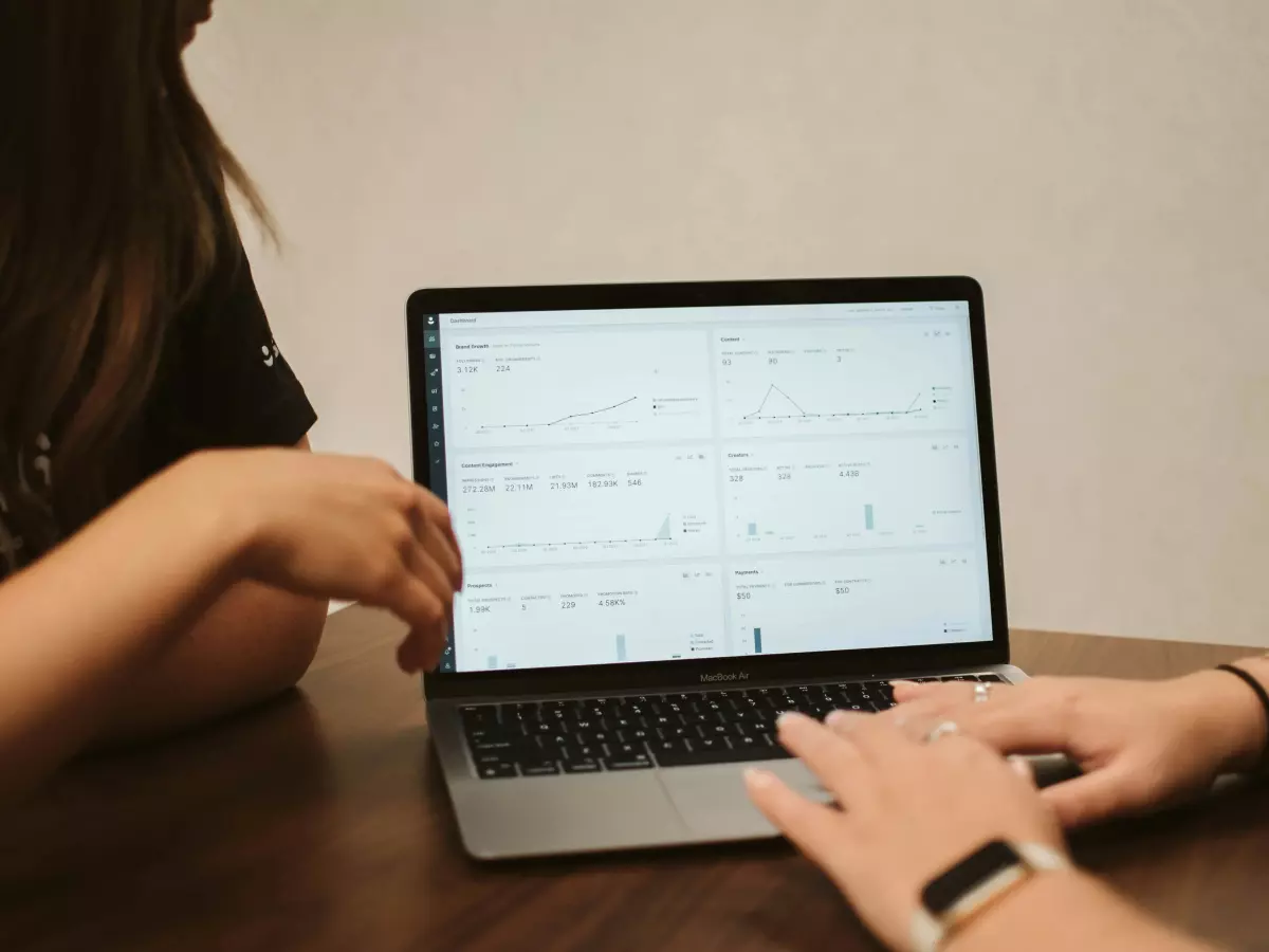 Two people looking at a laptop screen displaying various data charts.