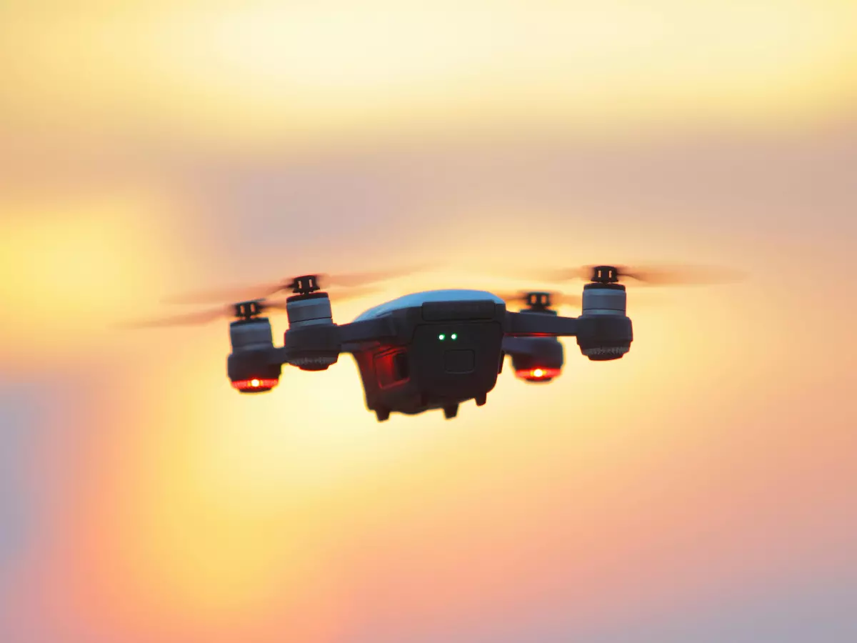 A black drone flies in the sky against a dramatic sunset background.