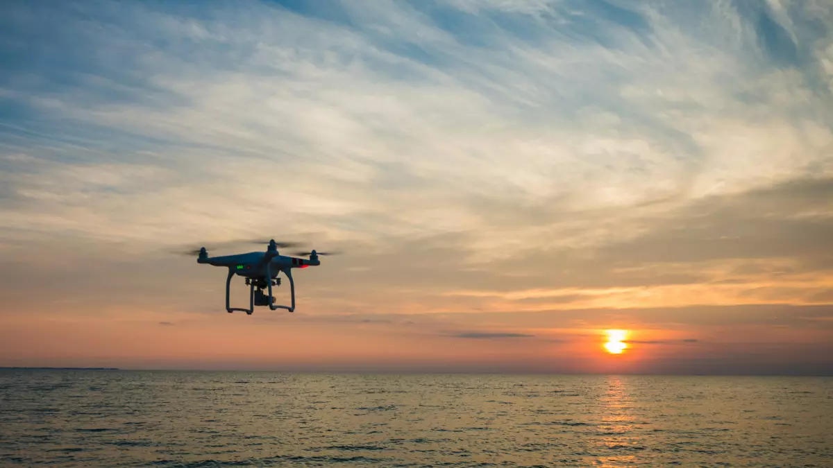 A drone flies over the ocean at sunset.