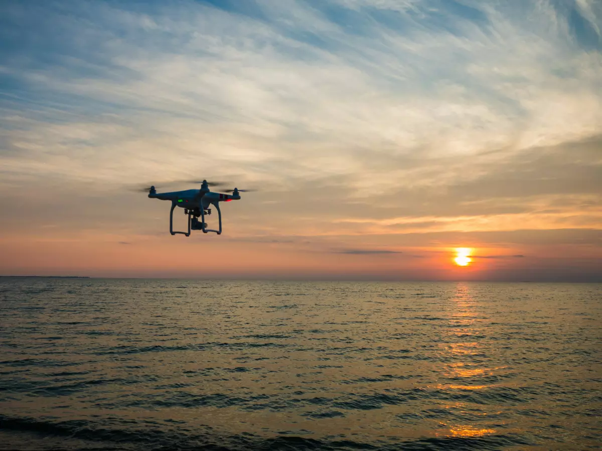 A drone flies over the ocean at sunset.