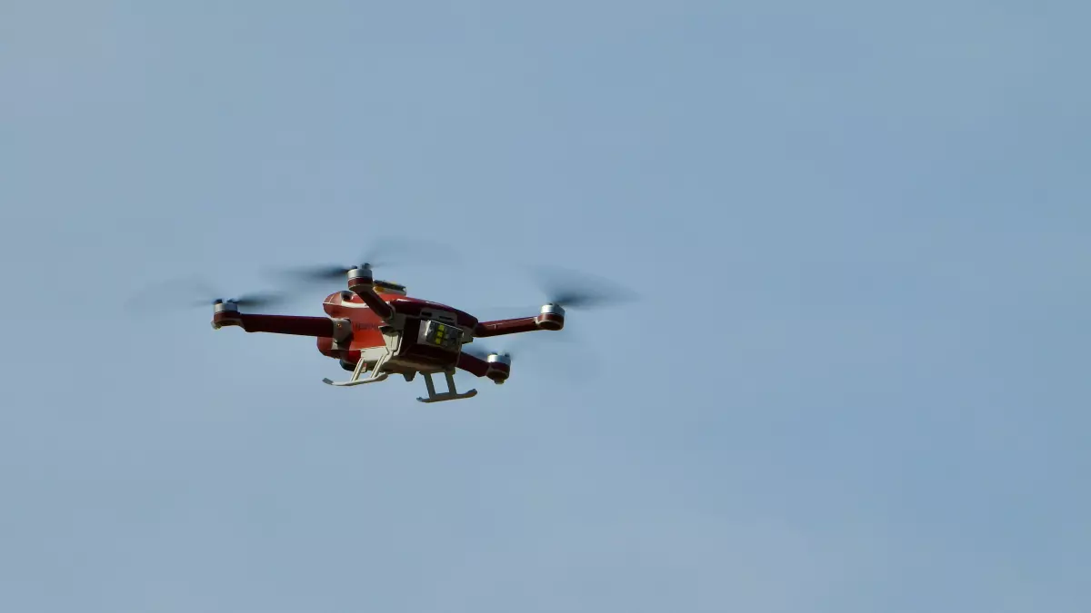 A red and white drone with four propellers flying in a blue sky.