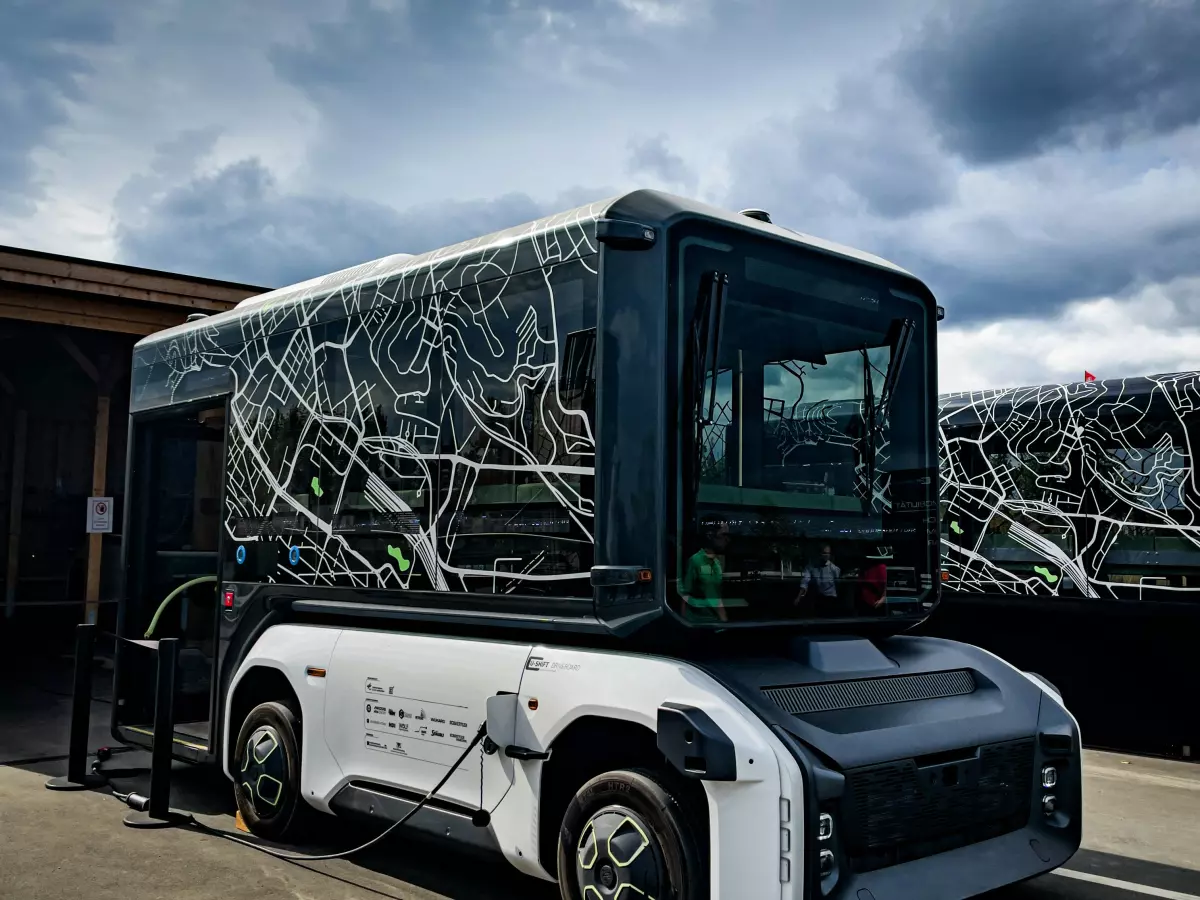 A white autonomous bus with a black roof is charging with a cable.