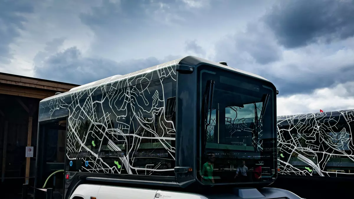 A white autonomous bus with a black roof is charging with a cable.