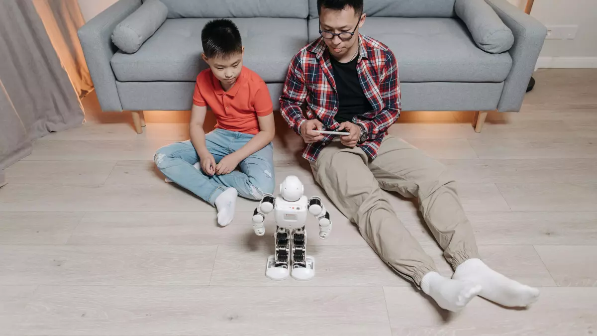 A young boy and a man are sitting on the floor, with a white robot between them.