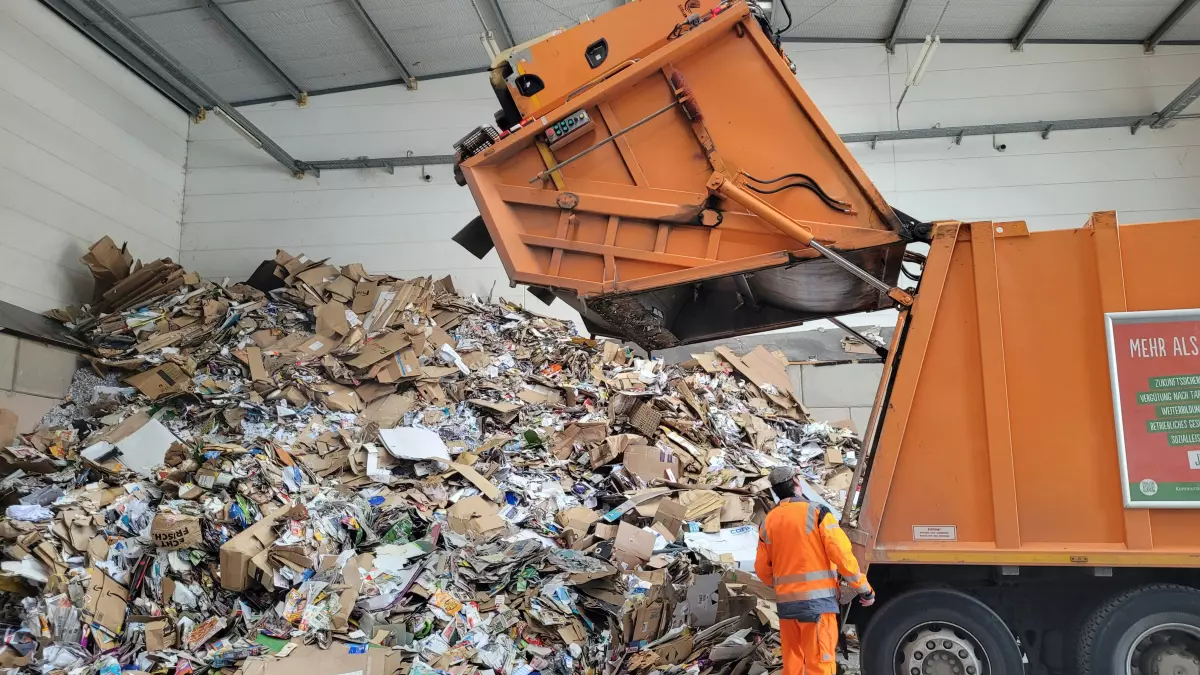 A garbage truck is collecting a large pile of cardboard and other recyclable materials.