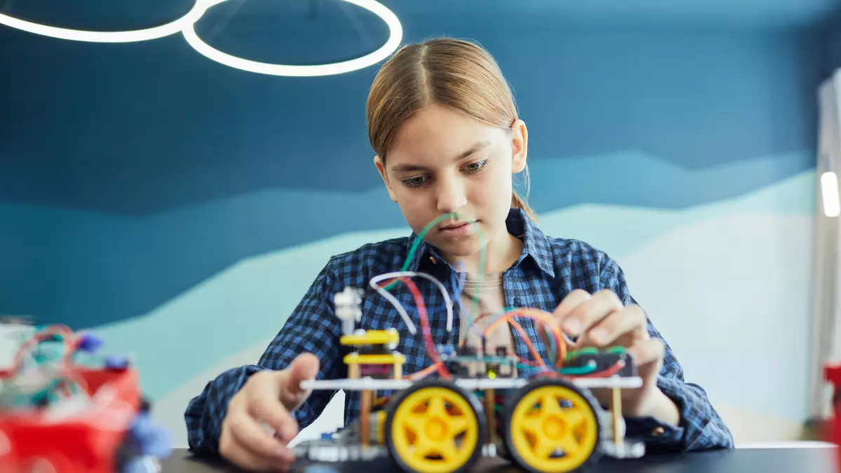 A young girl meticulously works on assembling a small robot, focusing intensely on the wiring.