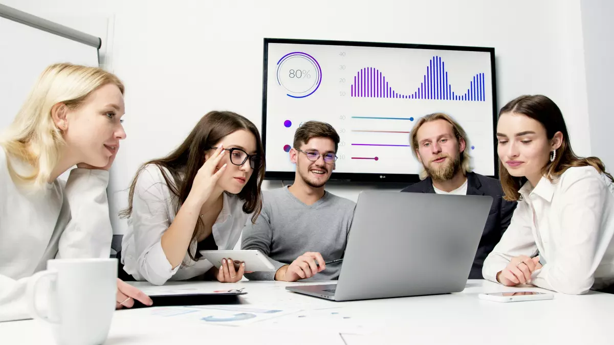 Four people are sitting around a table looking at a laptop