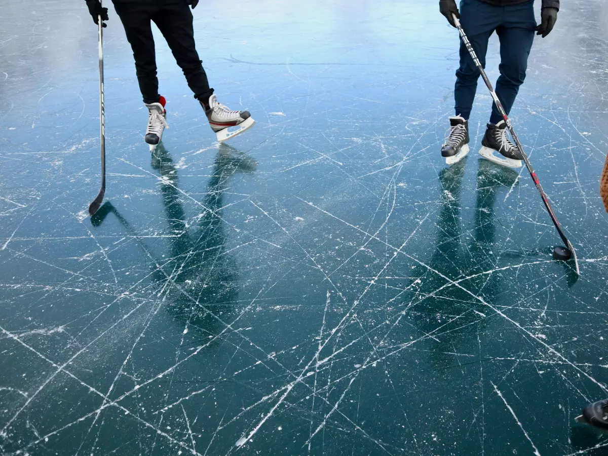 A group of people ice skating on a frozen lake, with their reflections clearly visible in the ice.