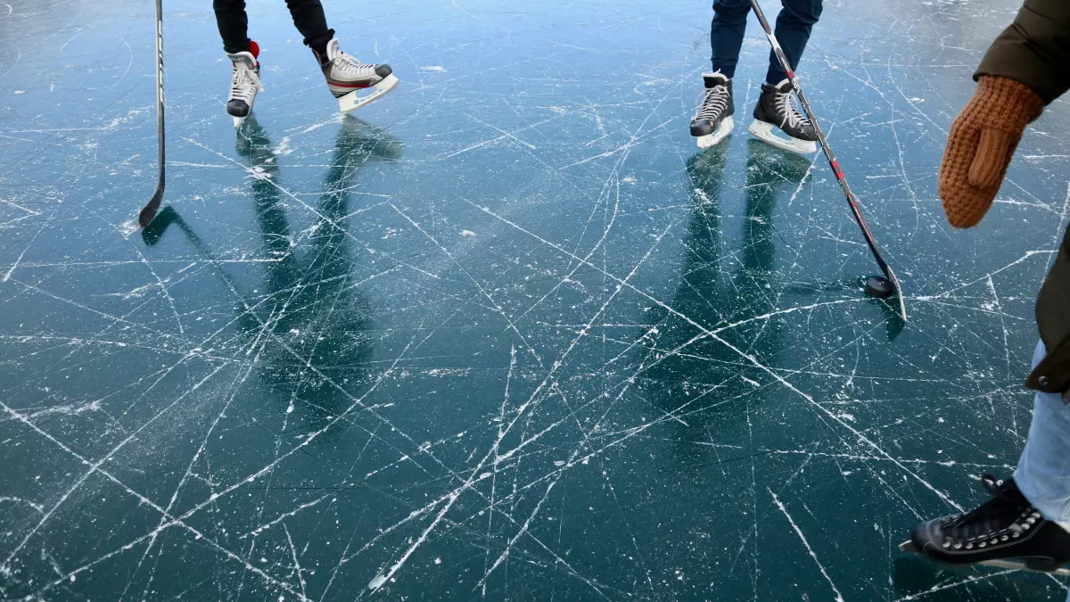 A group of people ice skating on a frozen lake, with their reflections clearly visible in the ice.