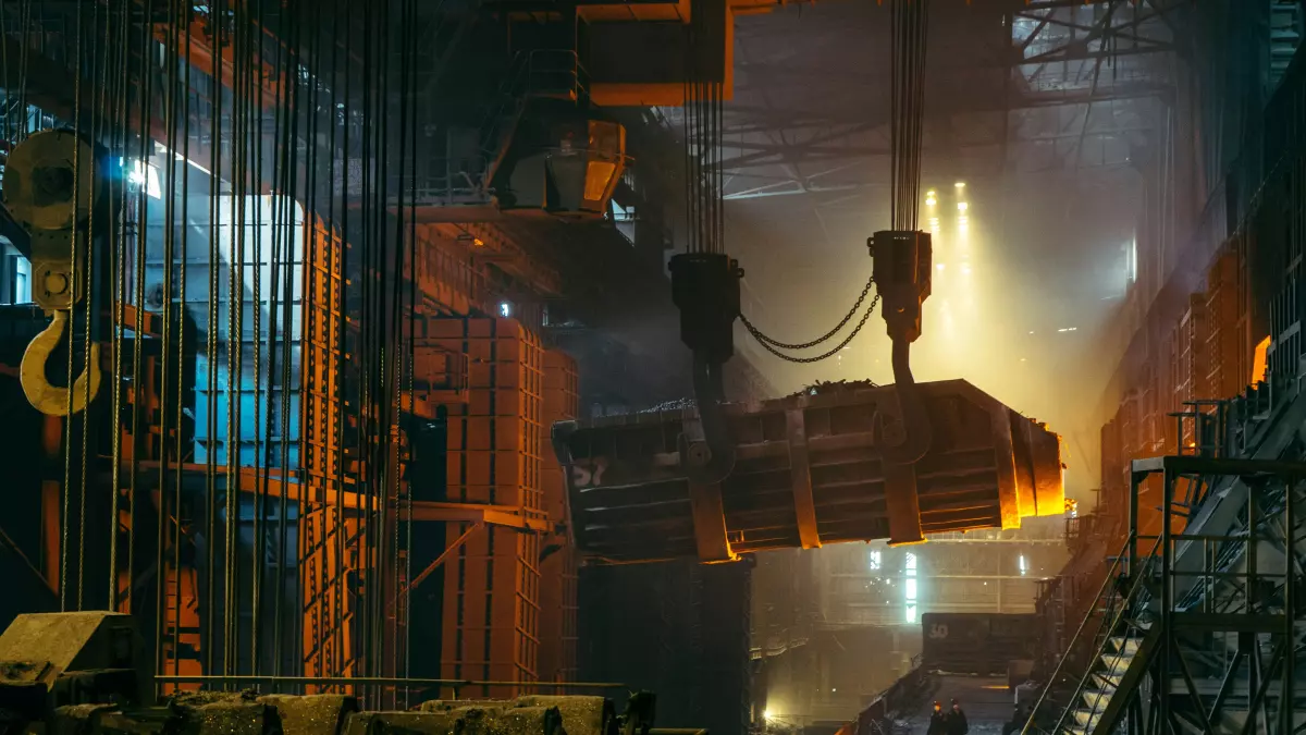 A large piece of metal being lifted by a crane in a factory.