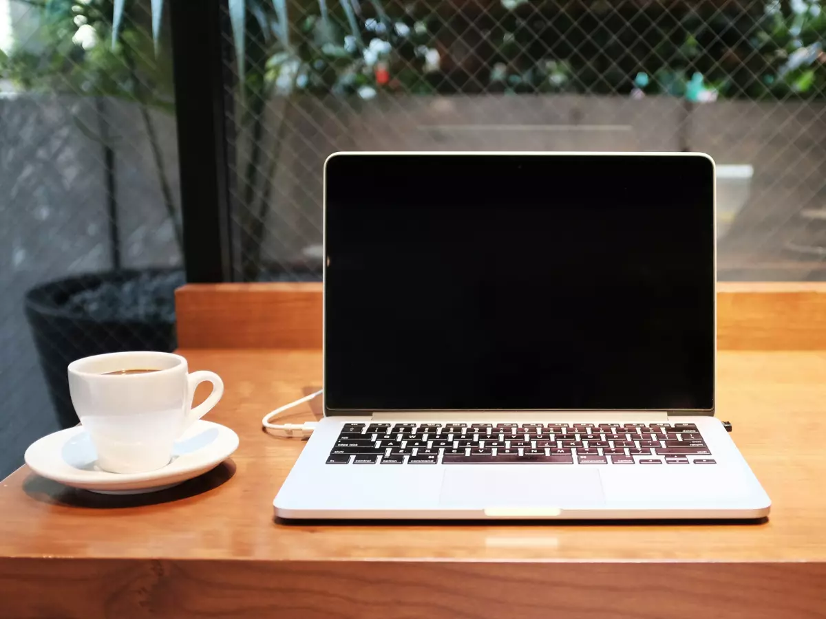 A laptop sits on a wooden table next to a cup of coffee.