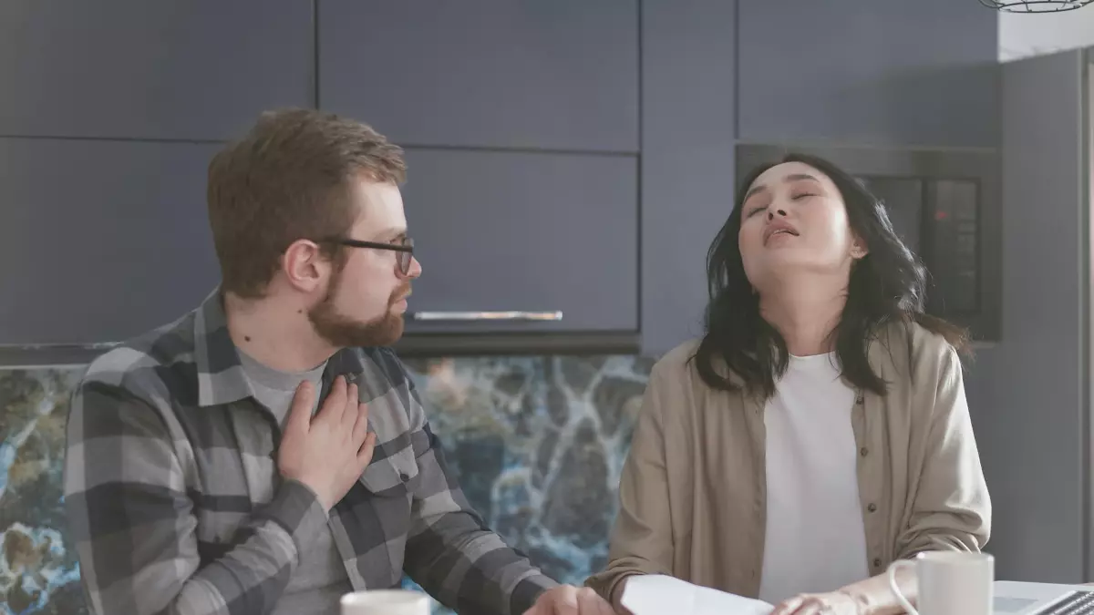 A couple sitting at a table with frustrated expressions on their faces, trying to connect a smart home device.