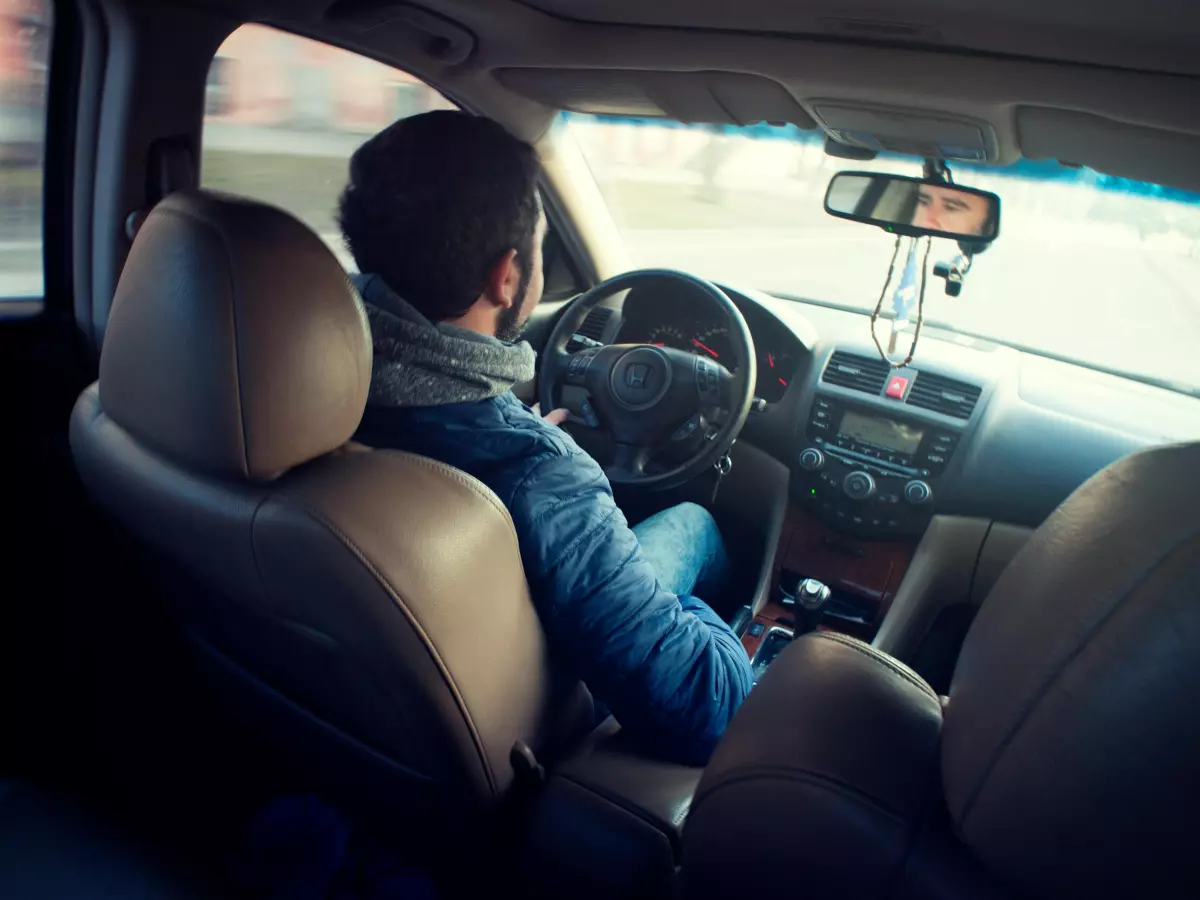 A man driving a car, seen from the rear passenger seat.