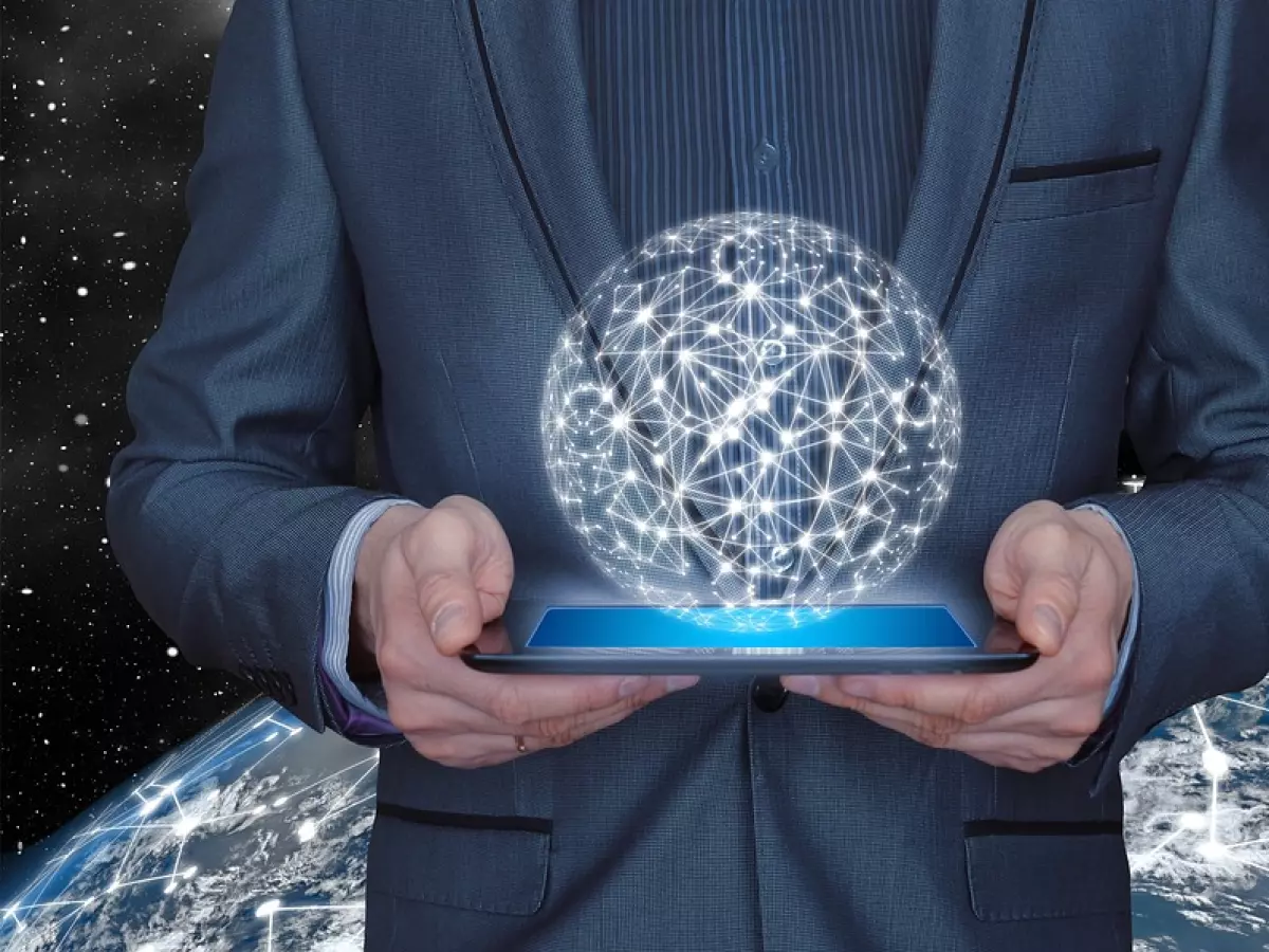 A man in a suit is holding a tablet with a holographic sphere of a network above it. The background shows the Earth with a similar network on its surface. The man is standing in front of a dark, starry sky.