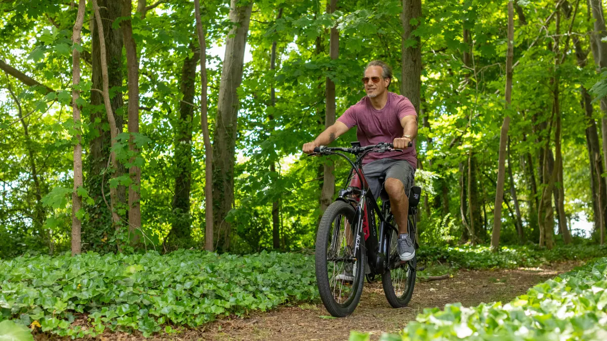 A man riding an electric bike on a dirt path in a forest.