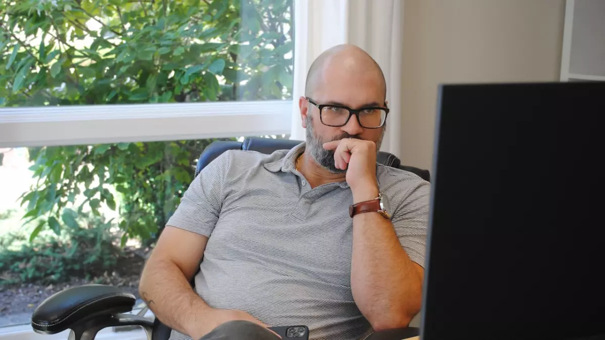 A man with a beard is sitting in an office chair, looking intently at a computer screen. He is contemplating something, perhaps about the role of loss functions in machine learning.