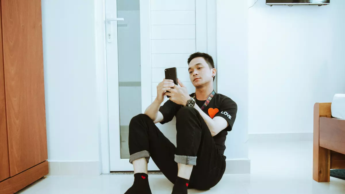 A young man sitting on the floor, using his smartphone.