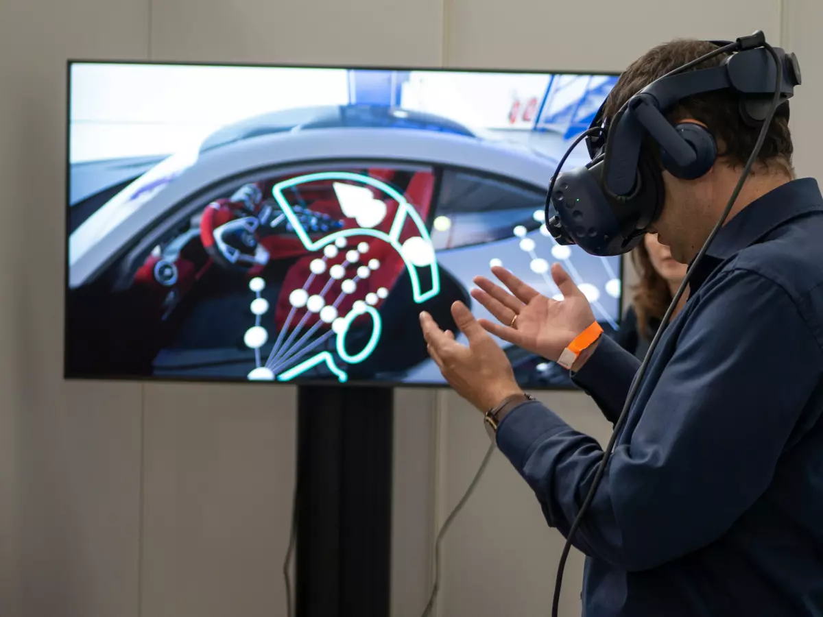 A man wearing VR goggles interacts with a screen showing virtual car interior data visualizations.