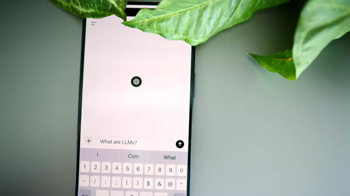 A smartphone displaying a text input screen with a keyboard; a leafy plant is partially obscuring the top of the screen.