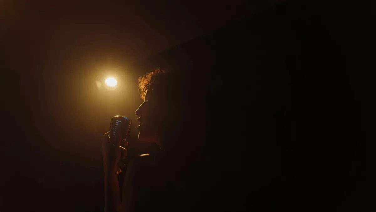 A person speaking into a microphone, with only their face and the microphone illuminated in a dark room.