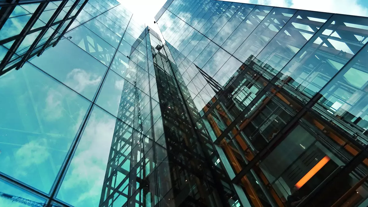 A low-angle shot of several skyscrapers, with the sky visible through their glass facades.