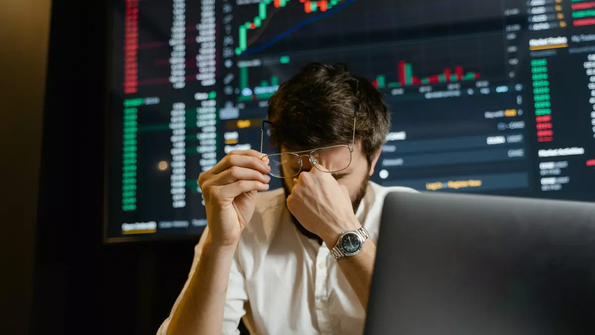 A man sitting in front of a computer screen, looking stressed and holding his head.