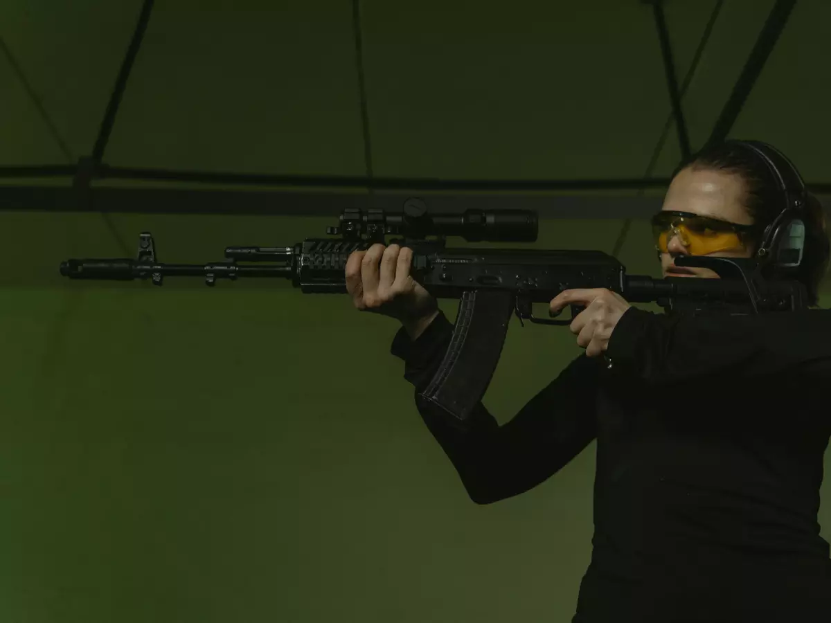 A woman in black clothing aiming a rifle at an indoor shooting range.