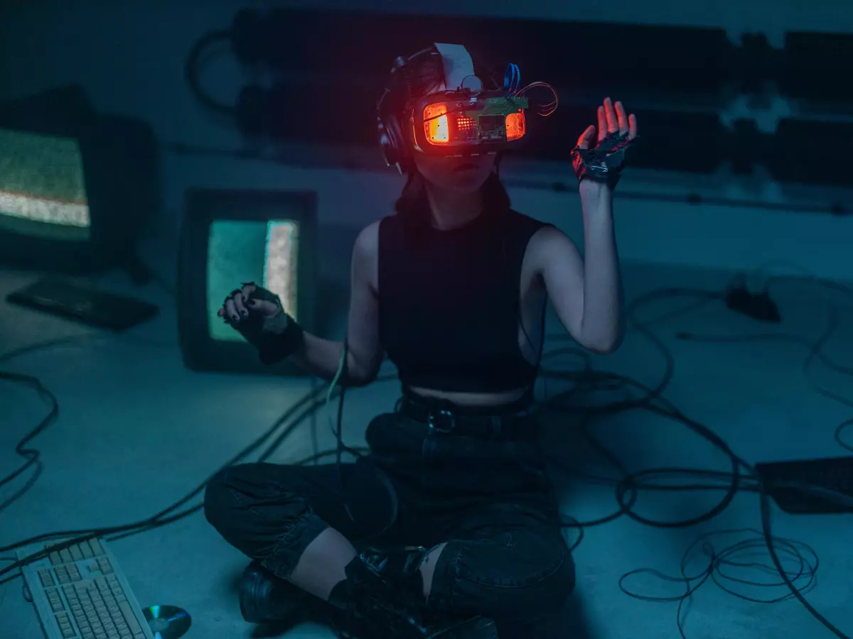 A person wearing a VR headset and gloves is sitting in front of multiple computer screens in a dark setting.