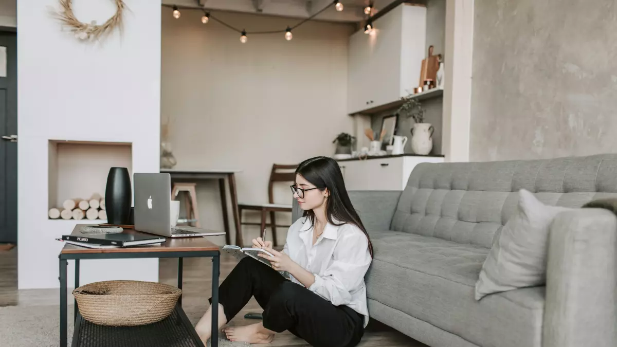 A young woman sits on the floor of a modern living room, using a laptop.  The room features muted colors and minimalist decor.